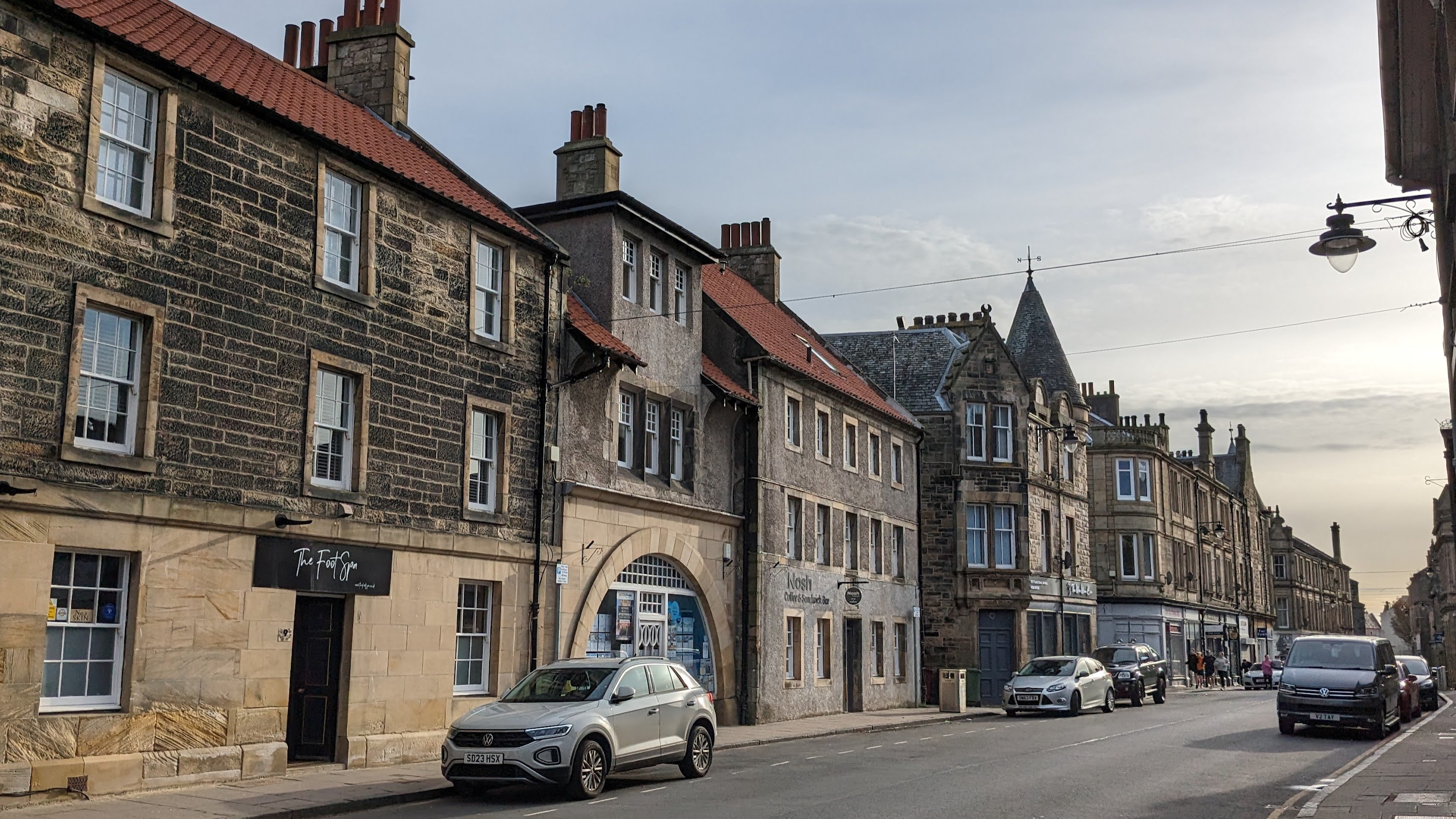 A street view of Bo'ness featuring traditional stone buildings, shops, and parked cars.