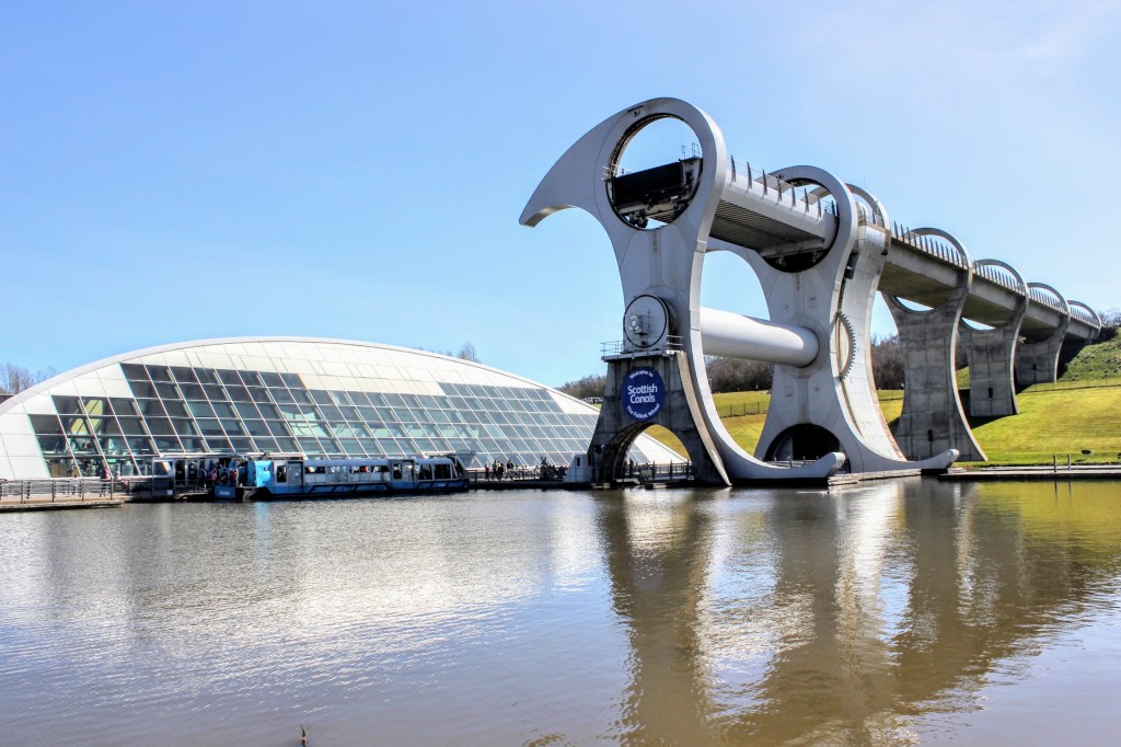 The Falkirk Wheel, a unique moving boat lift in Scotland, with a contemporary design, situated beside a waterway under a clear blue sky.