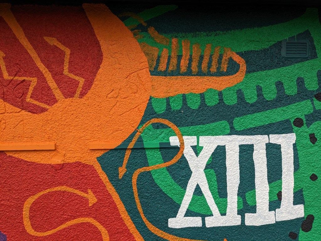 A vibrant mural featuring Roman-inspired designs, including a depiction of the numeral XII and abstract shapes in red, orange, and green colors.